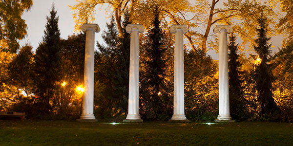 Trees backlit by sunshine with 4 Roman columns in front